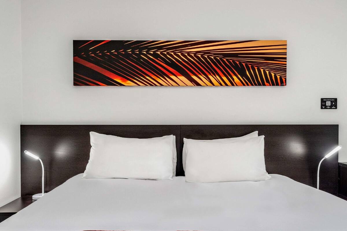 Une chambre d’hôtel avec un grand lit, deux lampes de chevet et une œuvre d’art moderne et abstraite accrochée au mur.