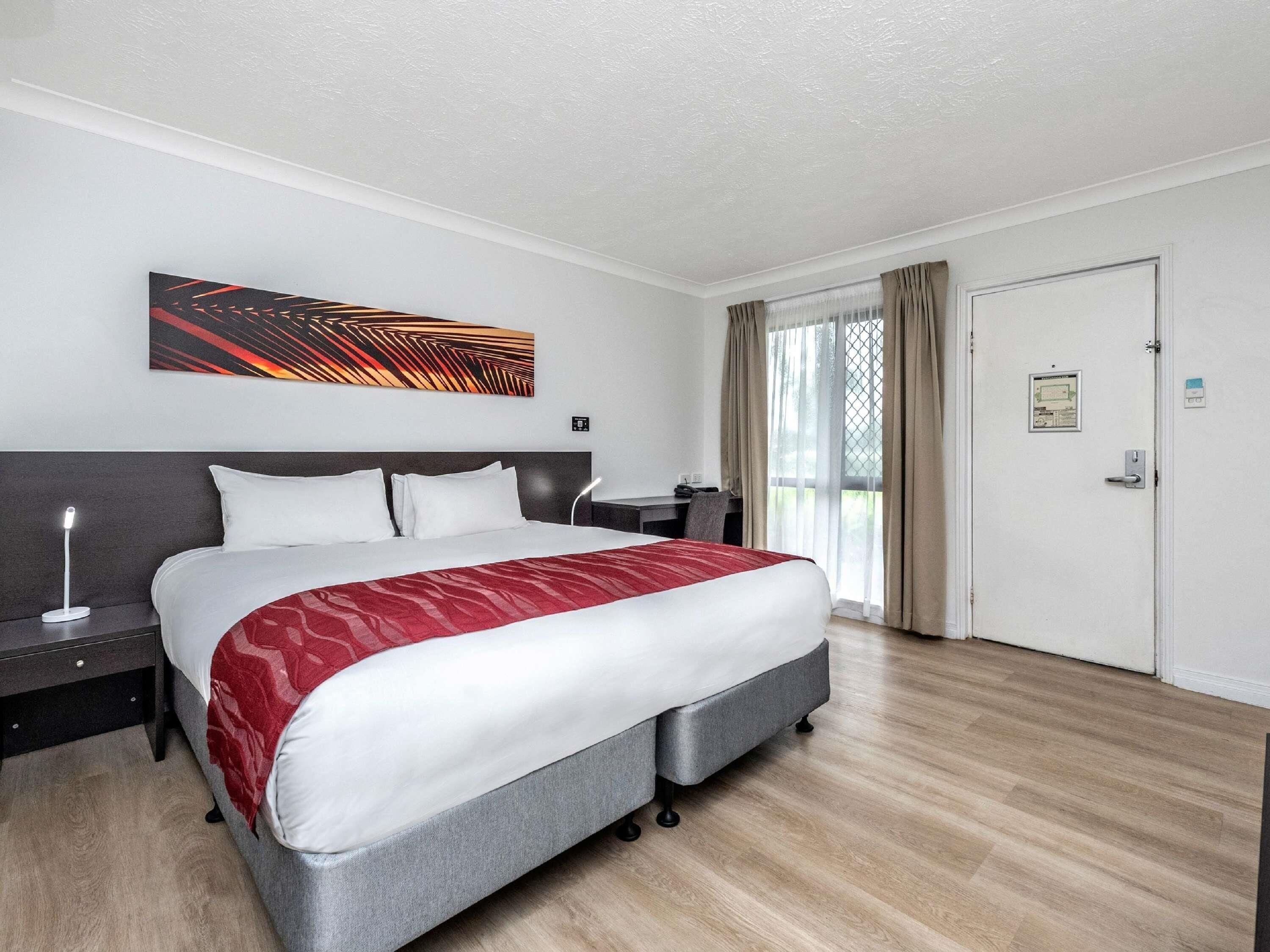 A hotel room with a bed, bedside table, lamp, and a large window with curtains.