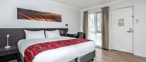 A hotel room with a bed, bedside table, lamp, and a large window with curtains.