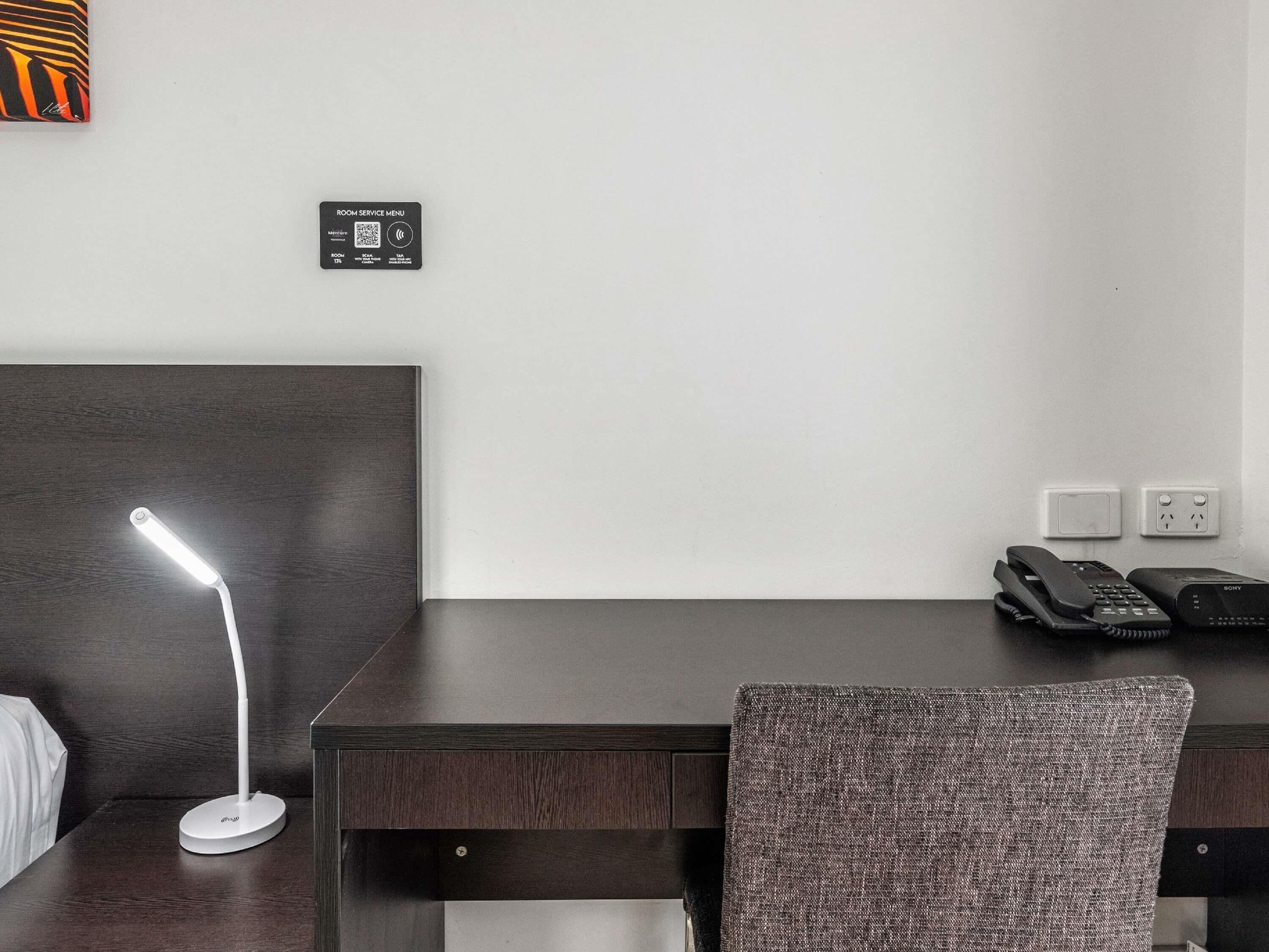 Habitación de hotel con escritorio, lámpara, teléfono y menú de servicios en la pared.