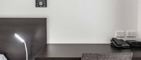 Habitación de hotel con escritorio, lámpara, teléfono y menú de servicios en la pared.