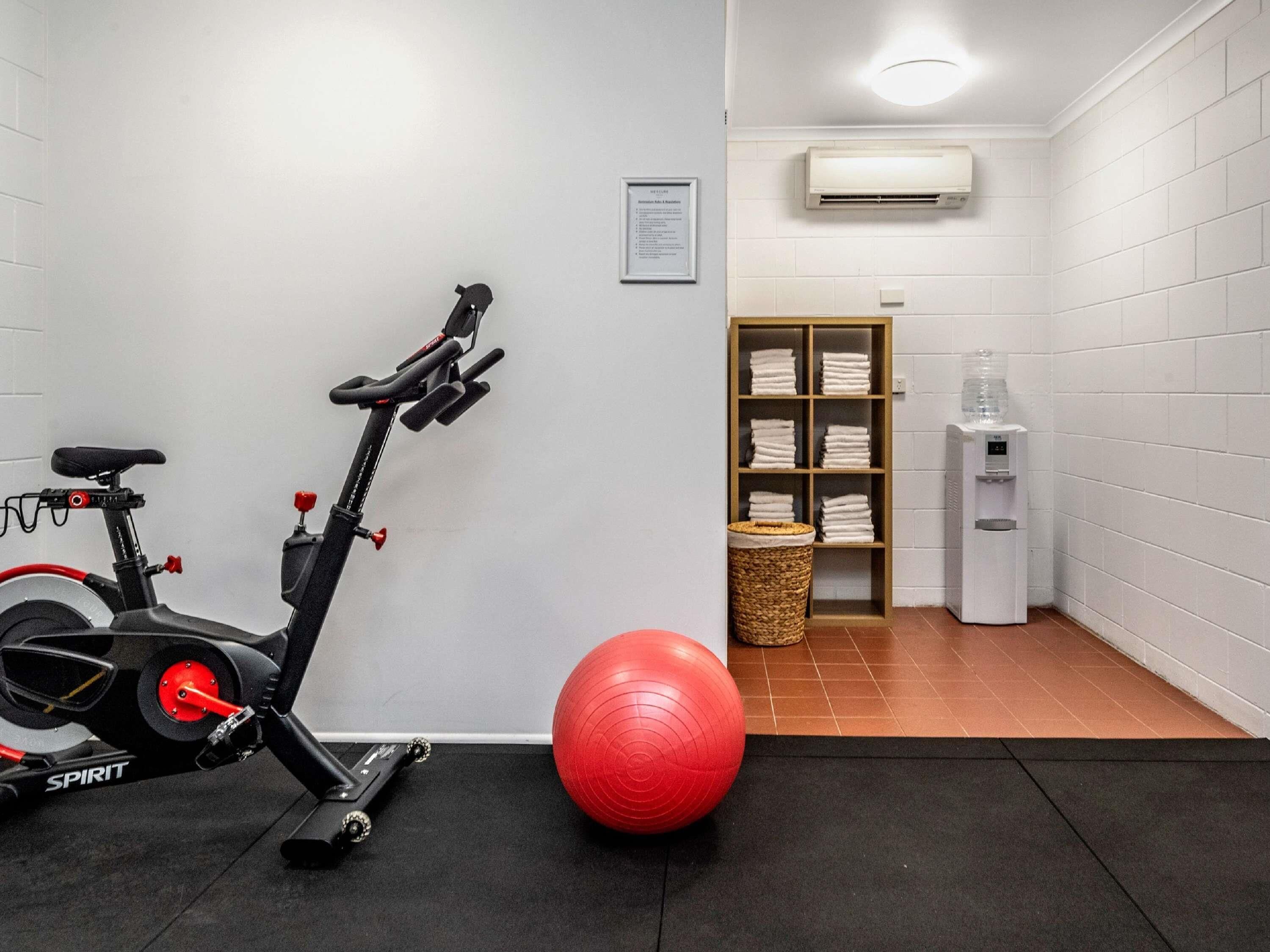 Ein Fitnessraum mit einem Ergometer, einem roten Trainingsball und einem Wasserspender.