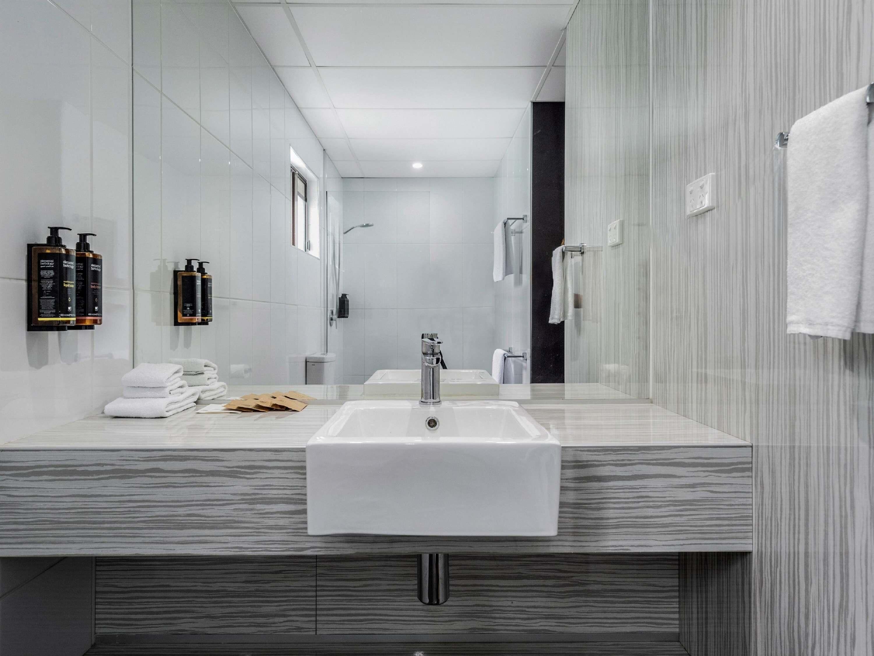 A modern bathroom with a large mirror, a sink, and a shower area.