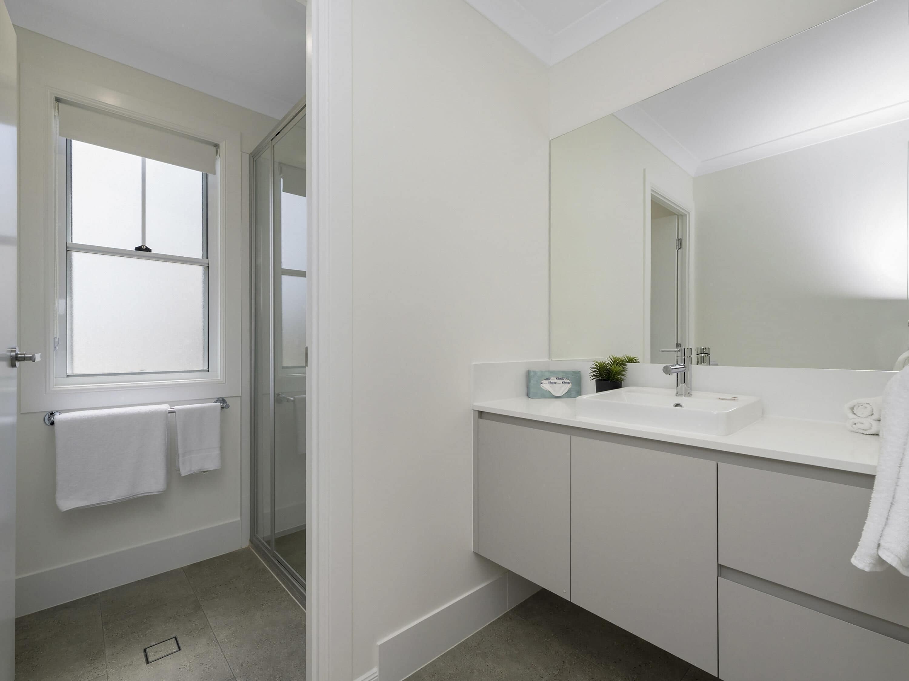 Un baño moderno con un espejo grande, armarios blancos y una ventana.