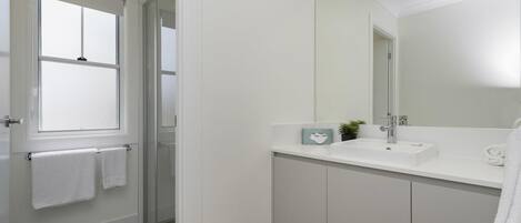 Un baño moderno con un espejo grande, armarios blancos y una ventana.