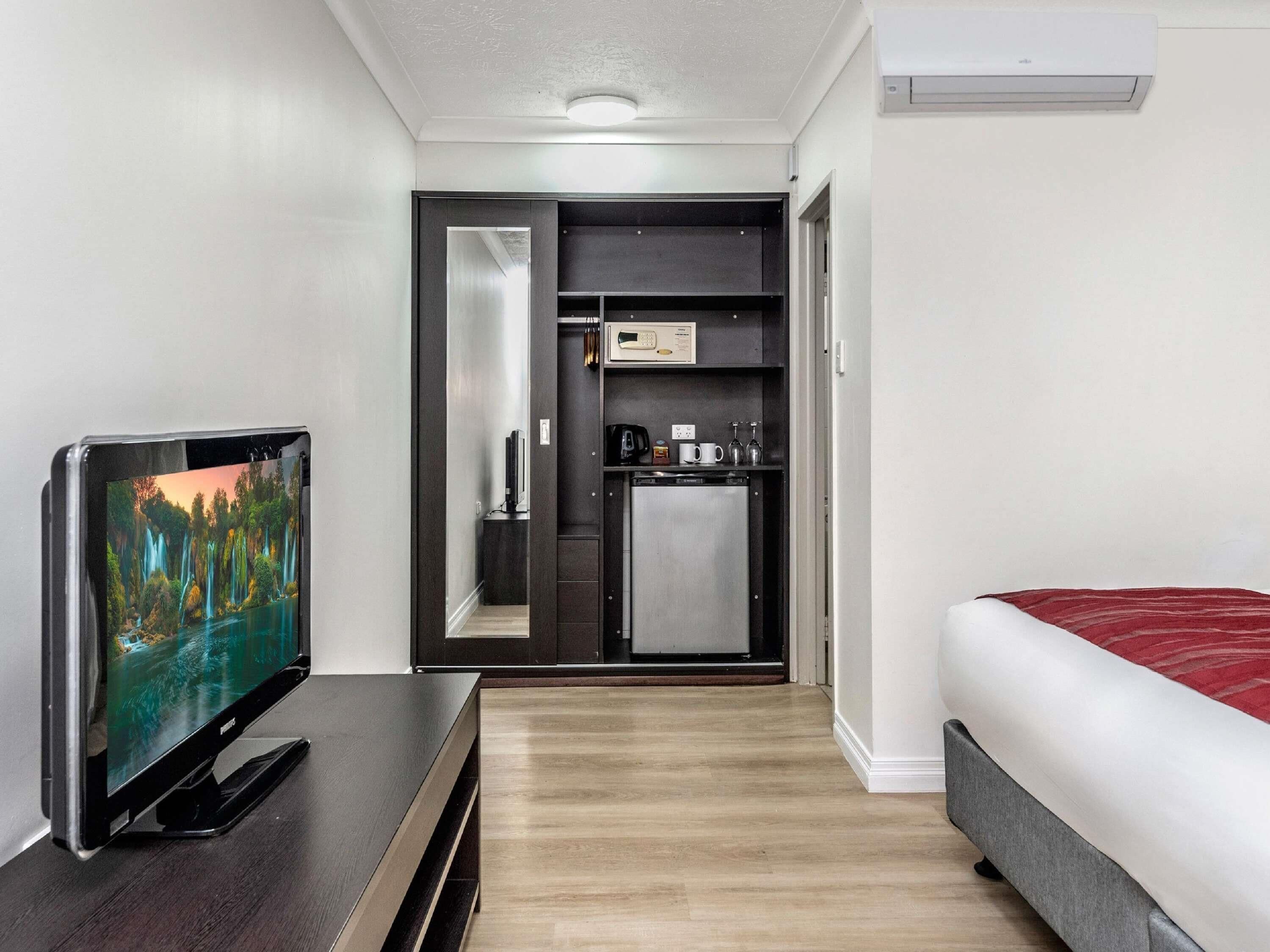 Habitación de hotel con cama, televisión, mini refrigerador, microondas y pequeña kitchenette.