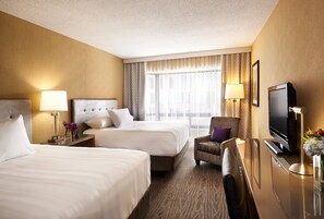 A hotel room with two beds, a desk, a television, and a window with curtains.