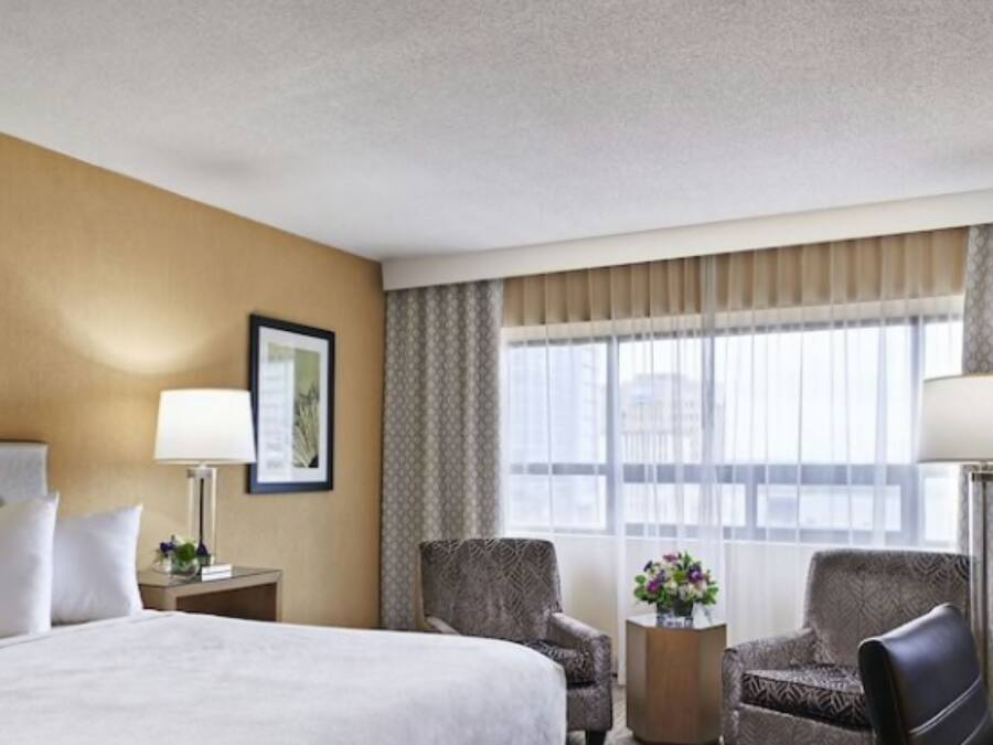 A hotel room with a large bed, two armchairs, a TV, and a window with curtains.