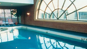 An indoor swimming pool with a large arched window, lounge chairs, and a brick wall.