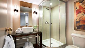 A modern bathroom with a glass-enclosed shower, a sink with a mirror above, and neatly rolled towels on a shelf.