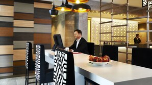 Een moderne hotellobby met een receptiebalie, zwart-wit gestreepte stoelen en een fruitschaal op de balie.