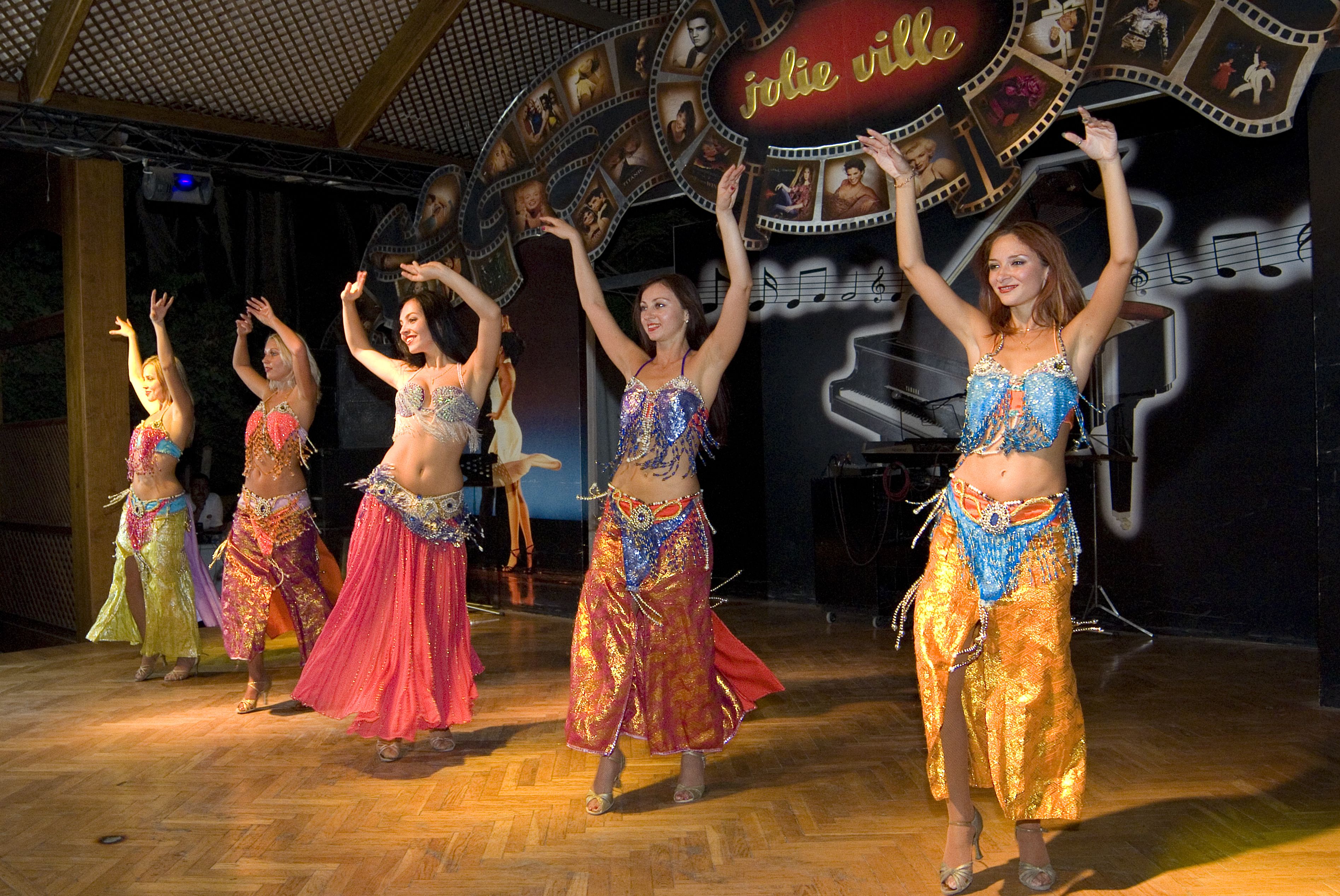 Une représentation de danse mettant en scène plusieurs danseurs vêtus de costumes colorés, sur une scène dotée d'un plancher en bois et d'un décor représentant des motifs inspirés de bandes de film.