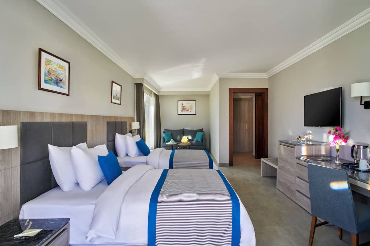 A hotel room with two beds, a desk, a TV, and a kitchenette.