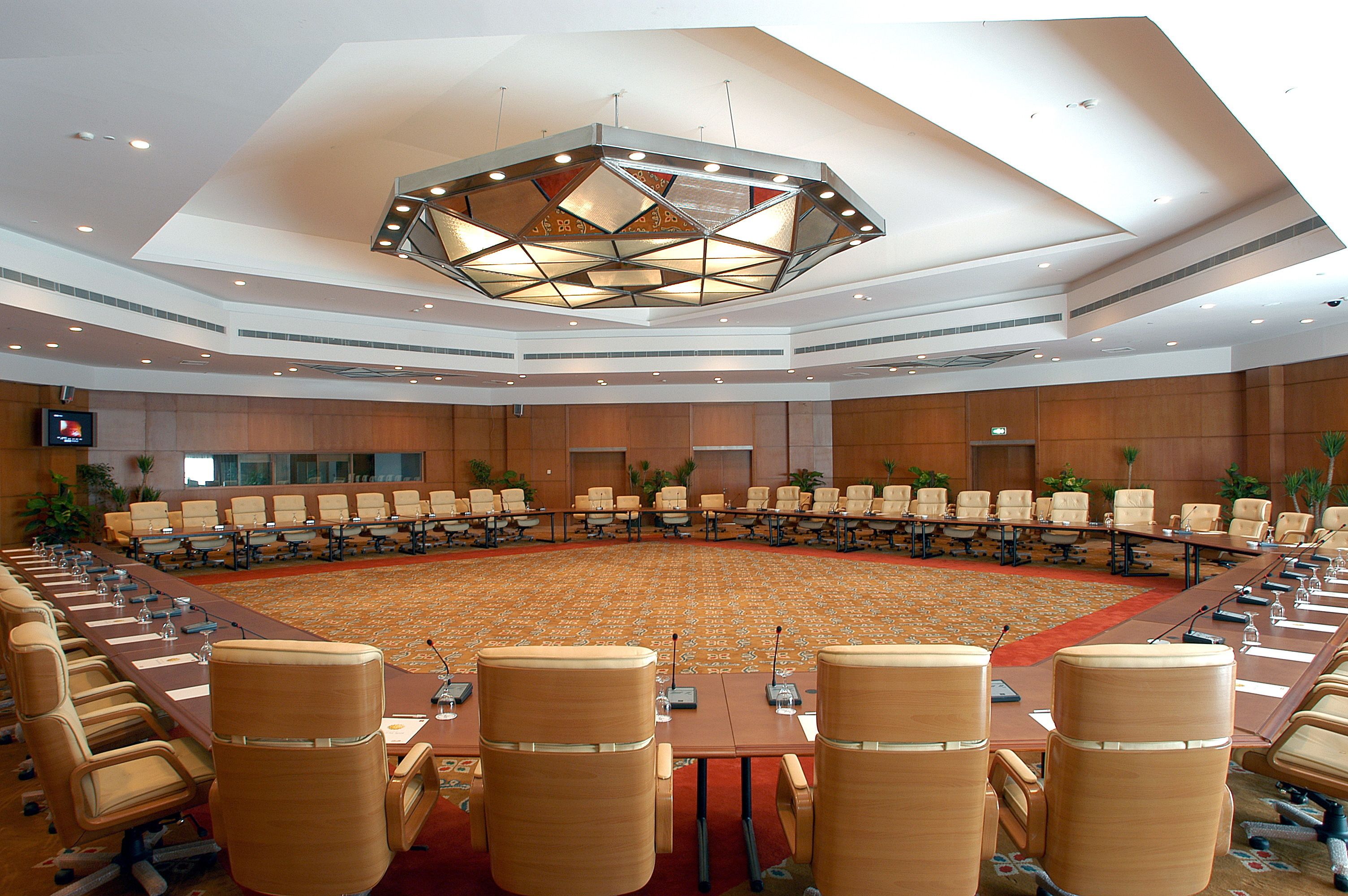 A large conference room with a long table and multiple chairs, equipped with microphones and water bottles.