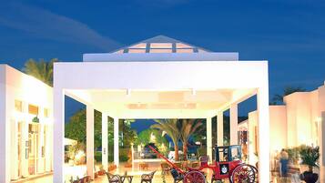 A covered outdoor area with a red horse-drawn carriage, palm trees, and a white building with columns.