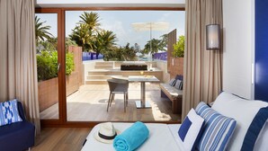 A hotel room with a bed, a sofa, a dining table with chairs, and a view of a pool and palm trees. - Hotel Son Caliu Spa Oasis (Calvia)