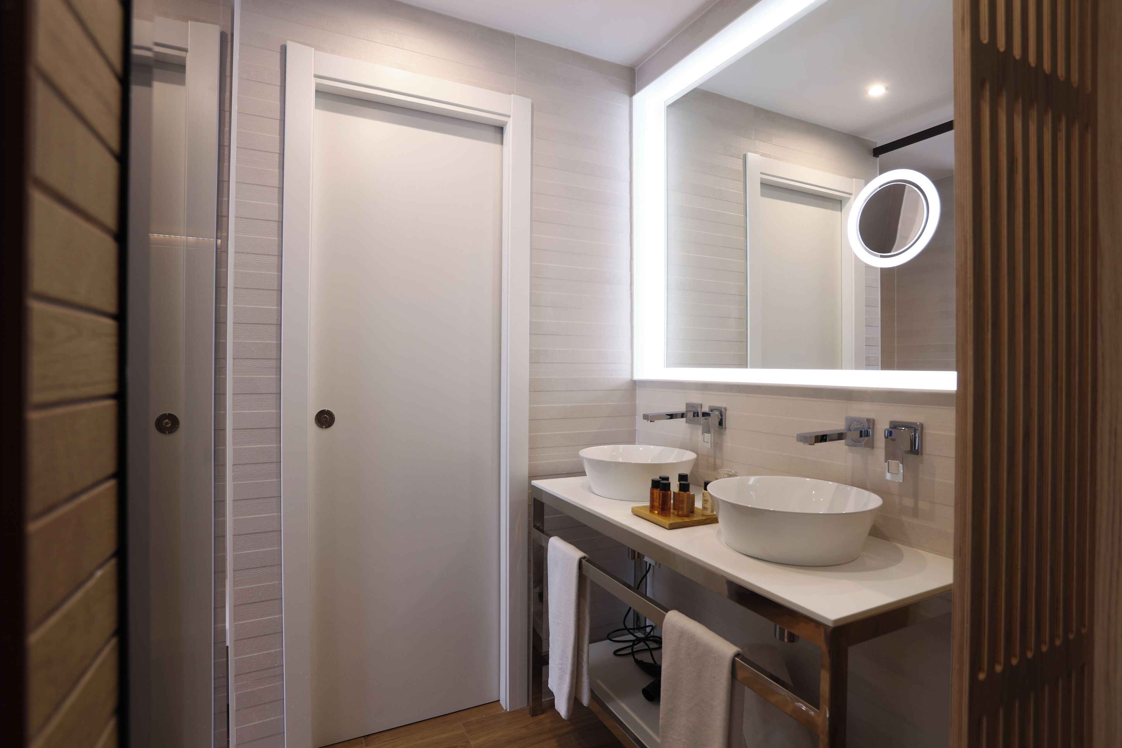 Een moderne badkamer met twee wastafels, een spiegel met verlichting en een houten deur.