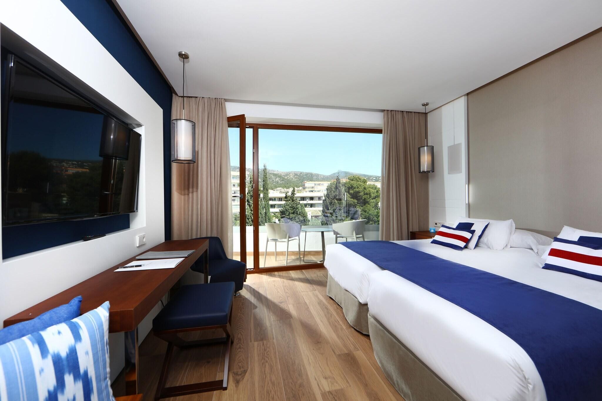 Ein Hotelzimmer mit Bett, Schreibtisch, Stuhl, Fernseher und einem Balkon mit Stadtblick.