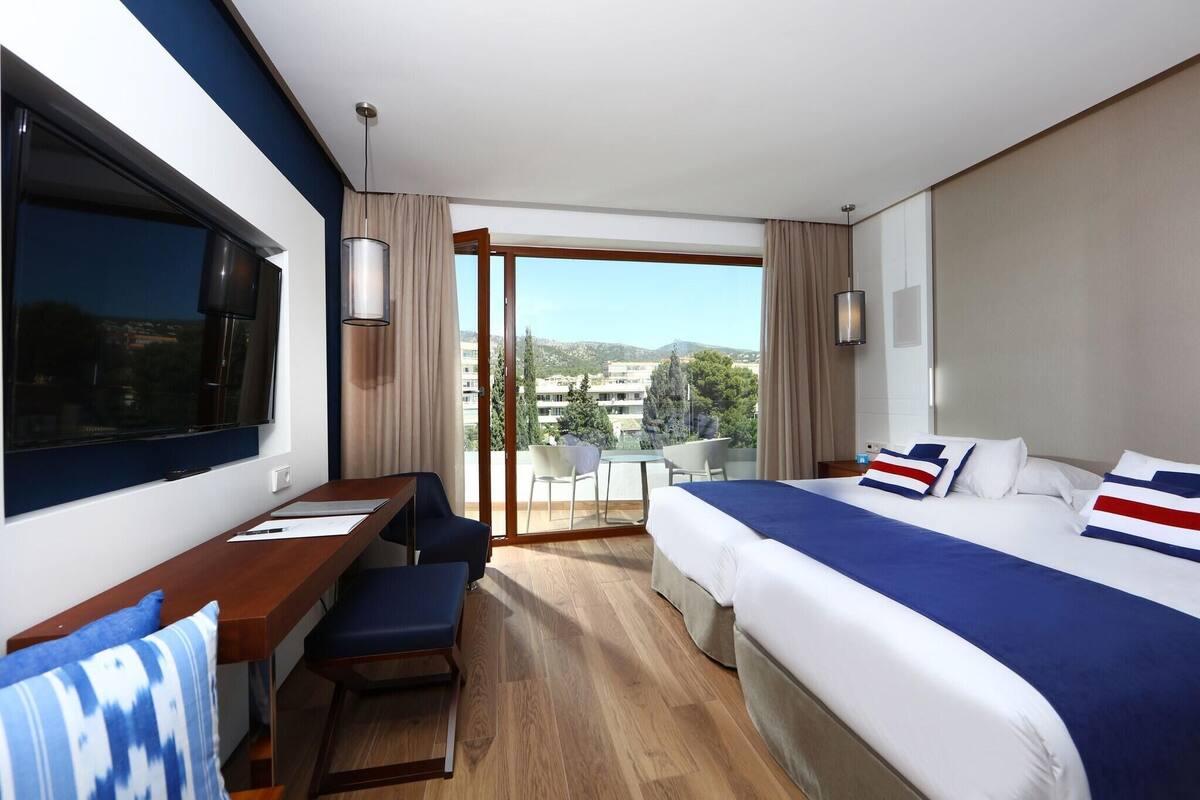 Hotelkamer met een bed, bureau, stoel, televisie en balkon met uitzicht op de stad.