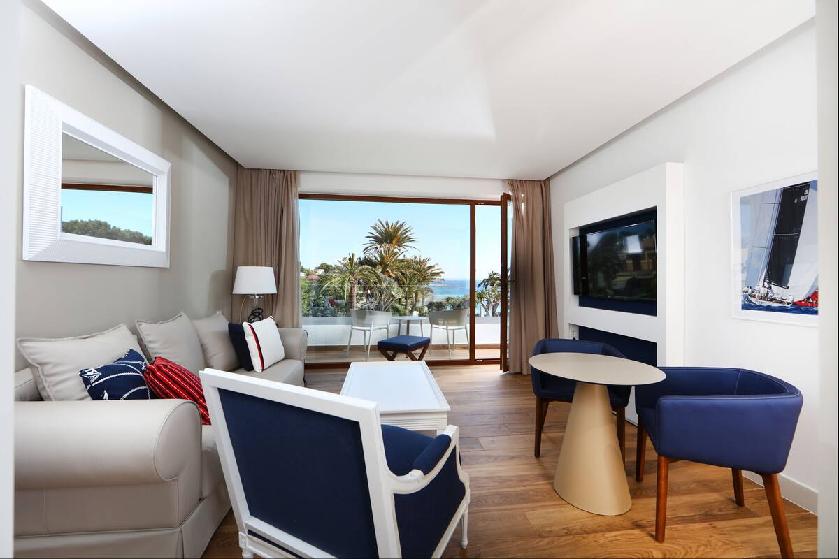 Een moderne hotelkamer met een bank, fauteuil, eettafel en een televisie.