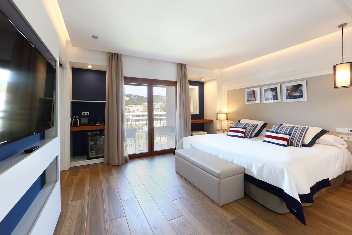 Een moderne hotelkamer met een groot bed, een televisie, een balkon met uitzicht over de stad en een minibar.