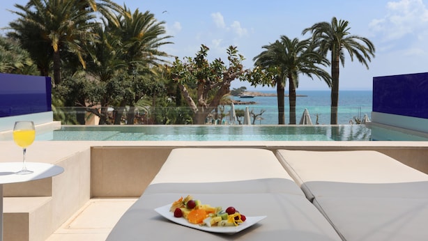 A poolside view with a plate of fruit and a glass of orange juice, overlooking a clear blue sea and palm trees. - Hotel Son Caliu Spa Oasis (Calvia)