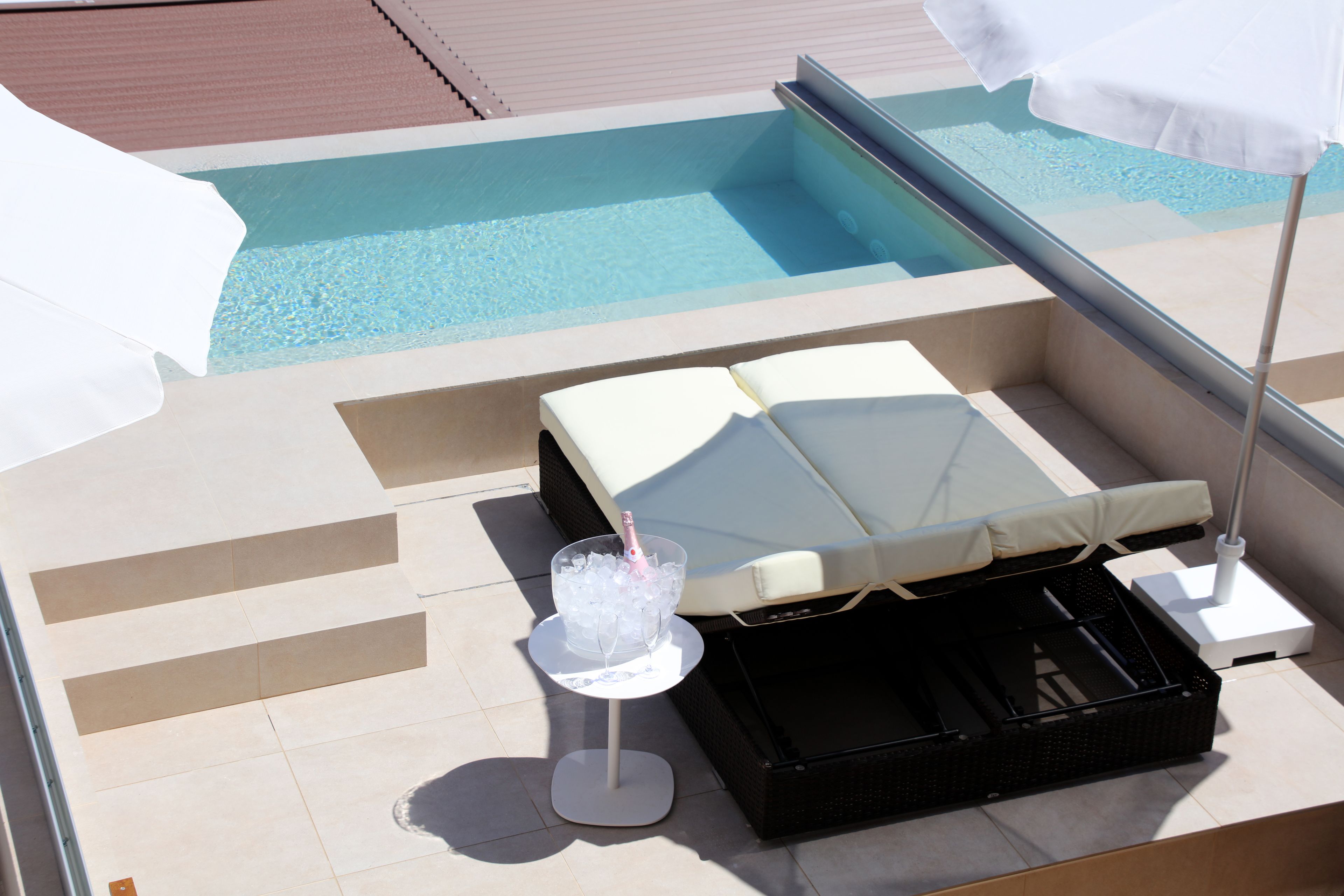 Ein Pool-Lounge-Bereich mit Liege, einem Getränk im Glas und einer Champagnerflasche.