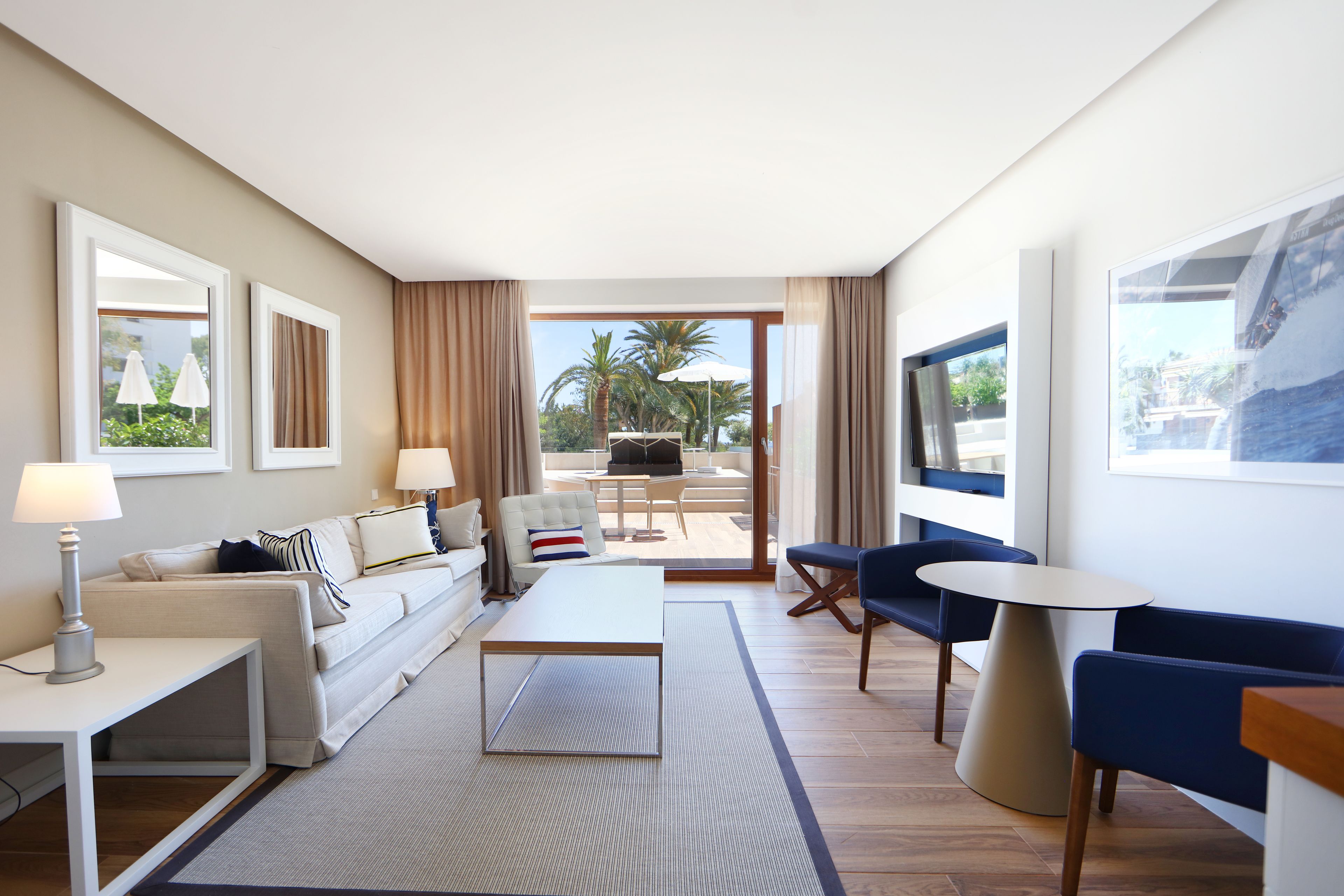 Habitación de hotel moderna con sofá, mesa de centro, televisión y balcón con mobiliario exterior.