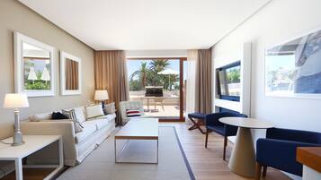 Habitación de hotel moderna con sofá, mesa de centro, televisión y balcón con mobiliario exterior.