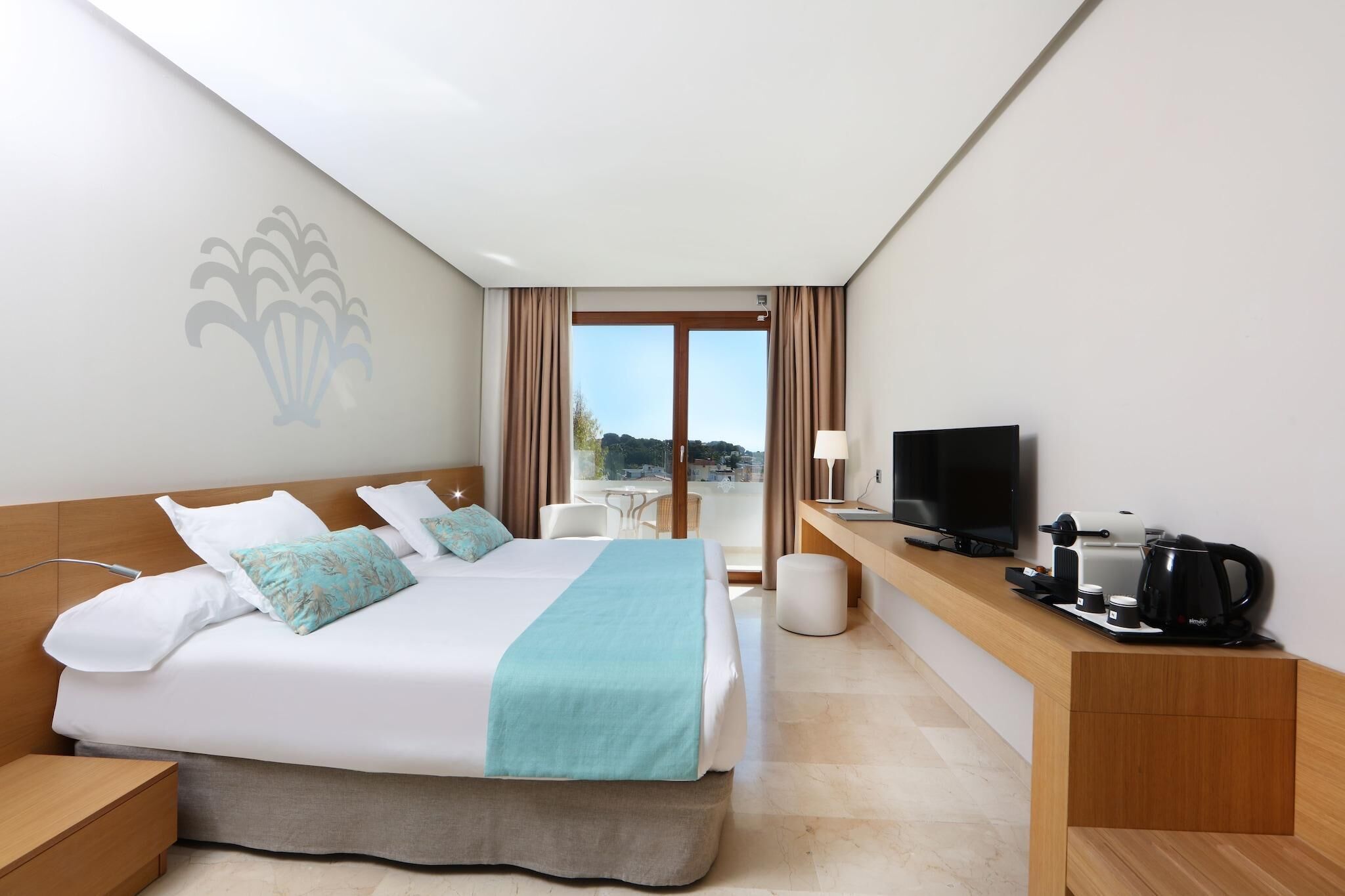 Ein Hotelzimmer mit Bett, Schreibtisch, Fernseher und Balkonblick.
