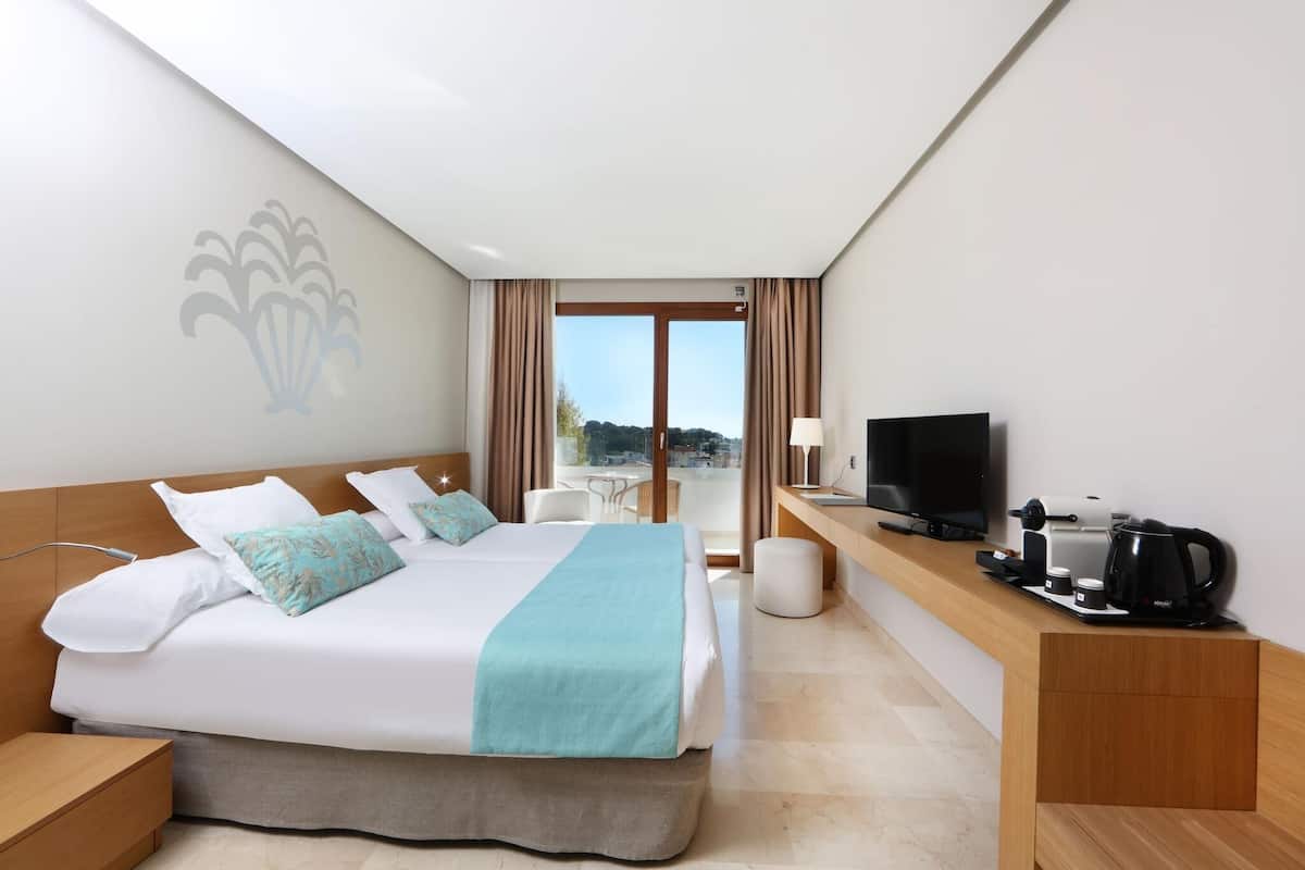 A hotel room with a bed, desk, TV, and balcony view.