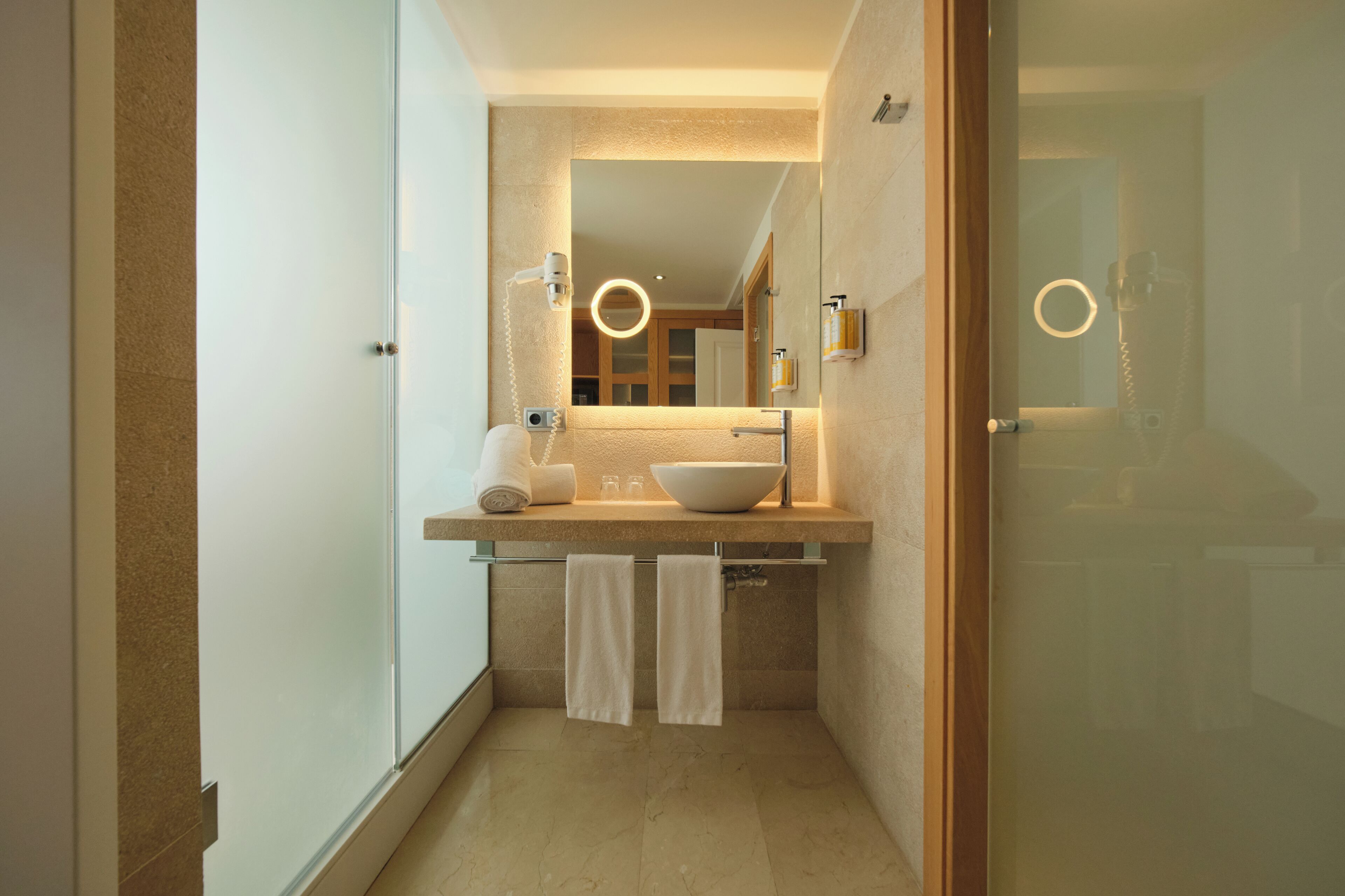 Un baño moderno con cabina de ducha de vidrio, un espejo grande y un mueble de tocador con lavabo y toallero.