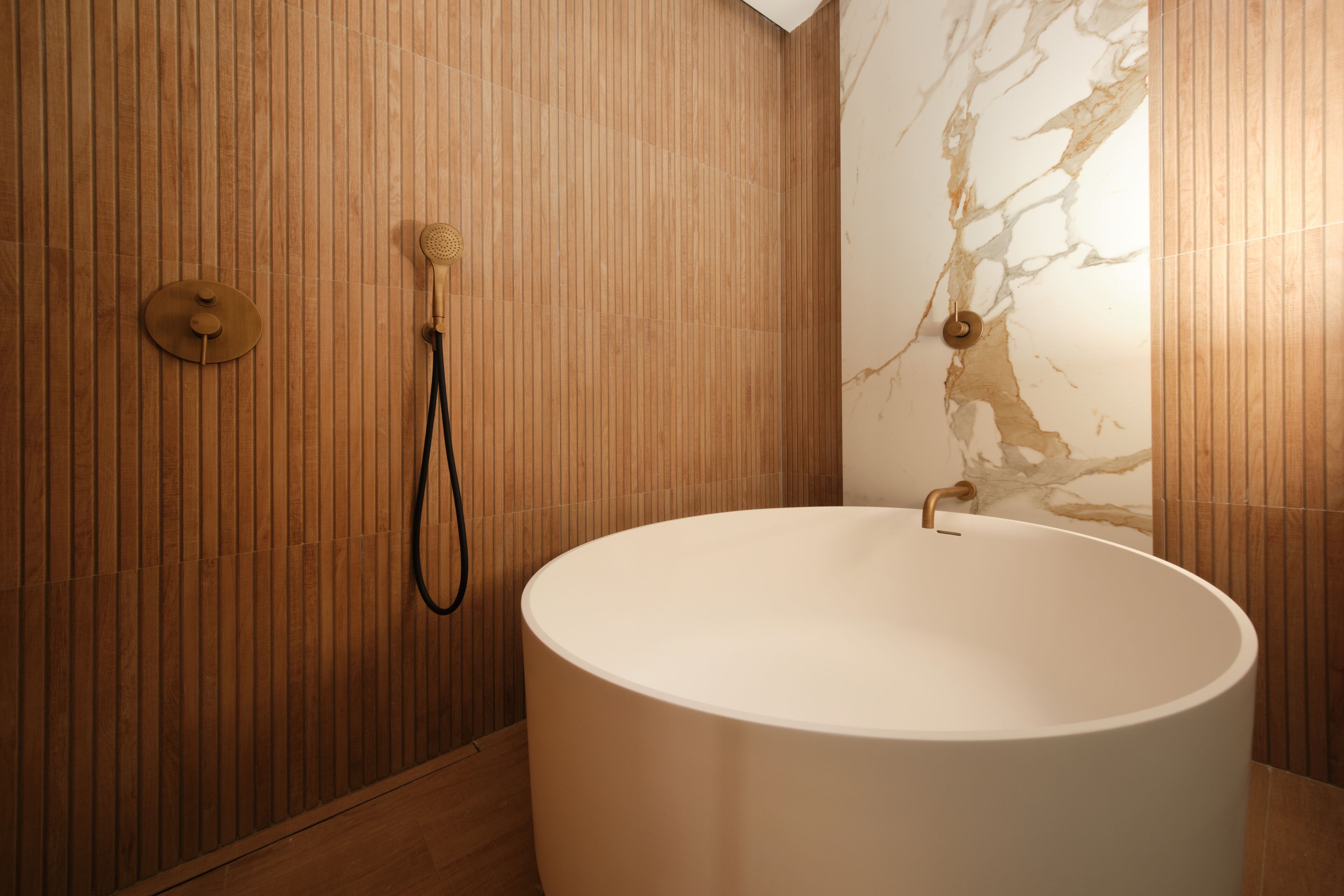 A modern bathroom with a large bathtub, wooden paneling, and a marble wall.