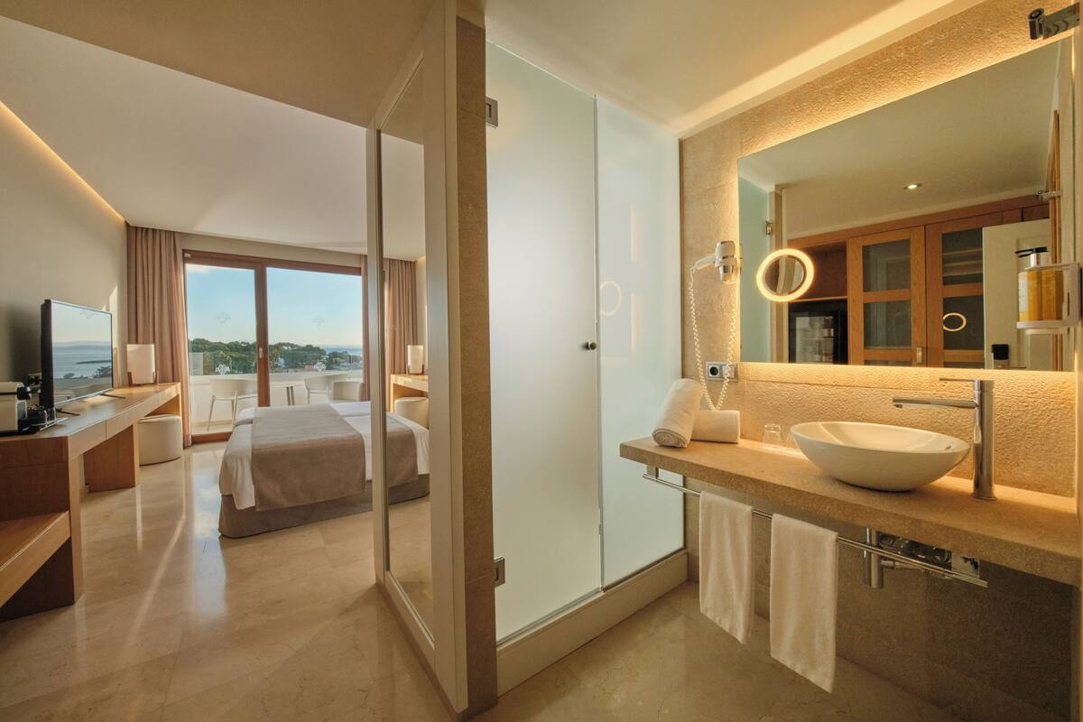 Een moderne hotelkamer met een groot bed, een bureau, een badkamer met een grote spiegel en uitzicht op de stad.