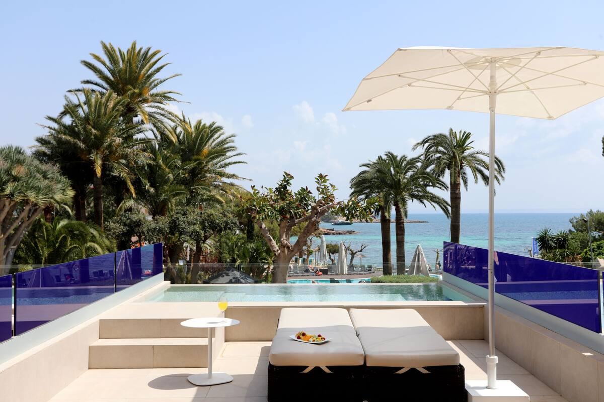 Een zwembadgedeelte met uitzicht op zee, een lounge met een tafel en stoelen en een parasol.