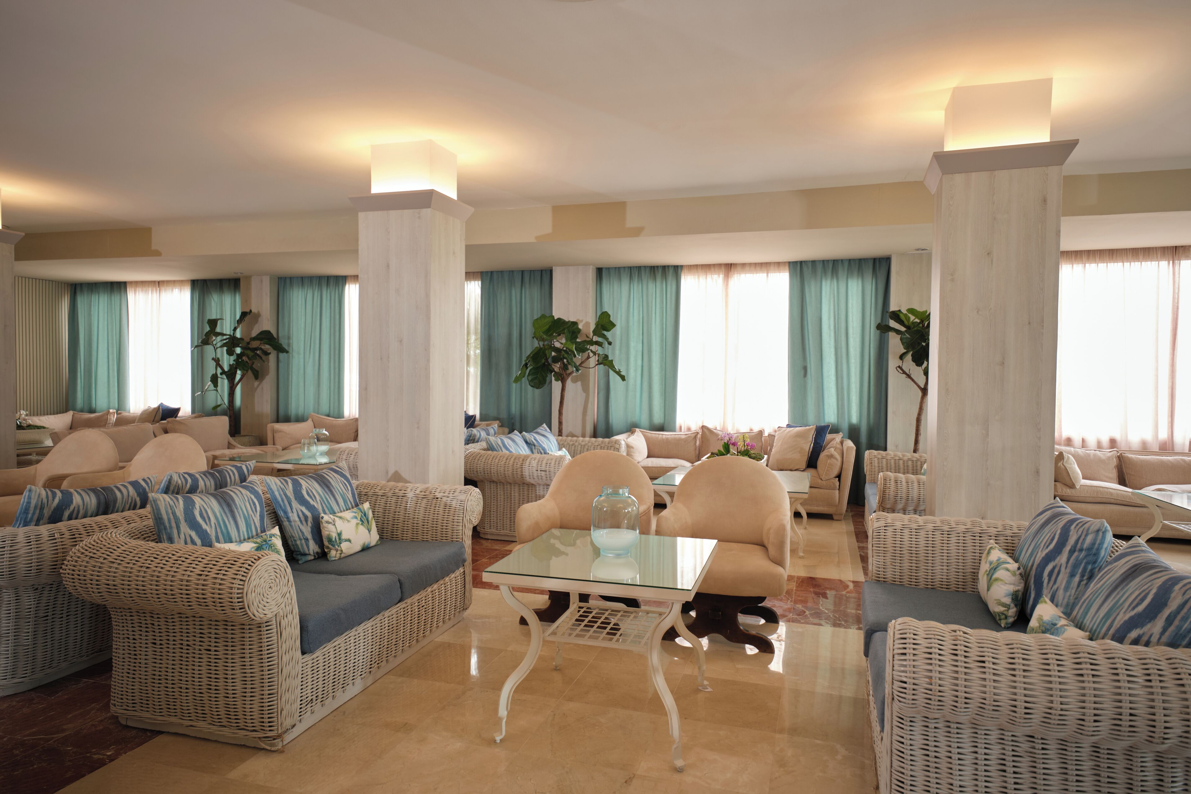 A spacious living room with wicker furniture, a glass coffee table, and large windows with curtains.