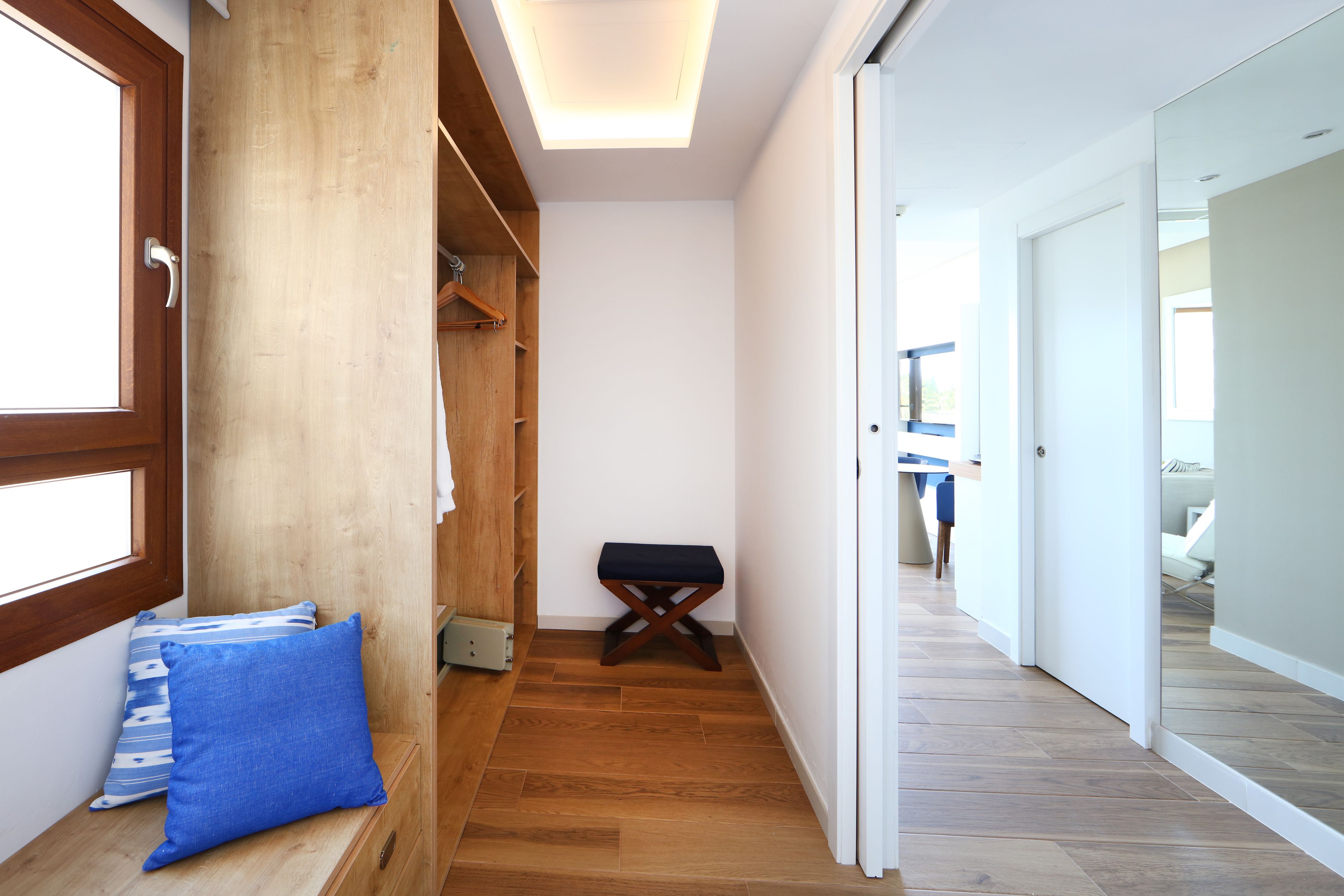 A narrow hallway with wooden flooring, a bench, and a wooden wardrobe.