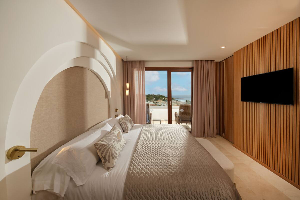 Een moderne hotelkamer met een groot bed, een aan de muur bevestigde televisie en uitzicht op zee.