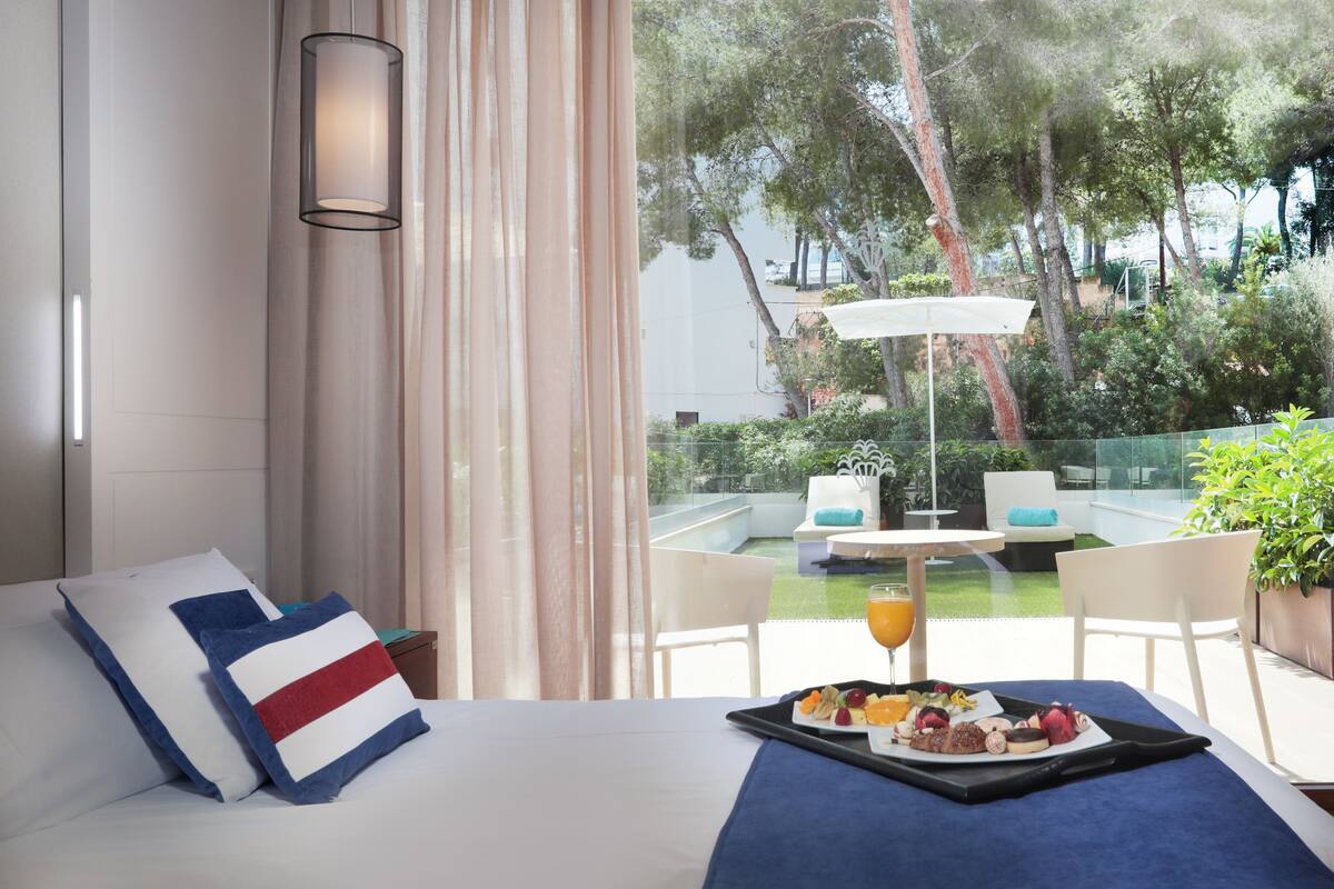 Een hotelkamer met een bed, een ontbijtplateau en uitzicht op een terras met een tafel en stoelen.