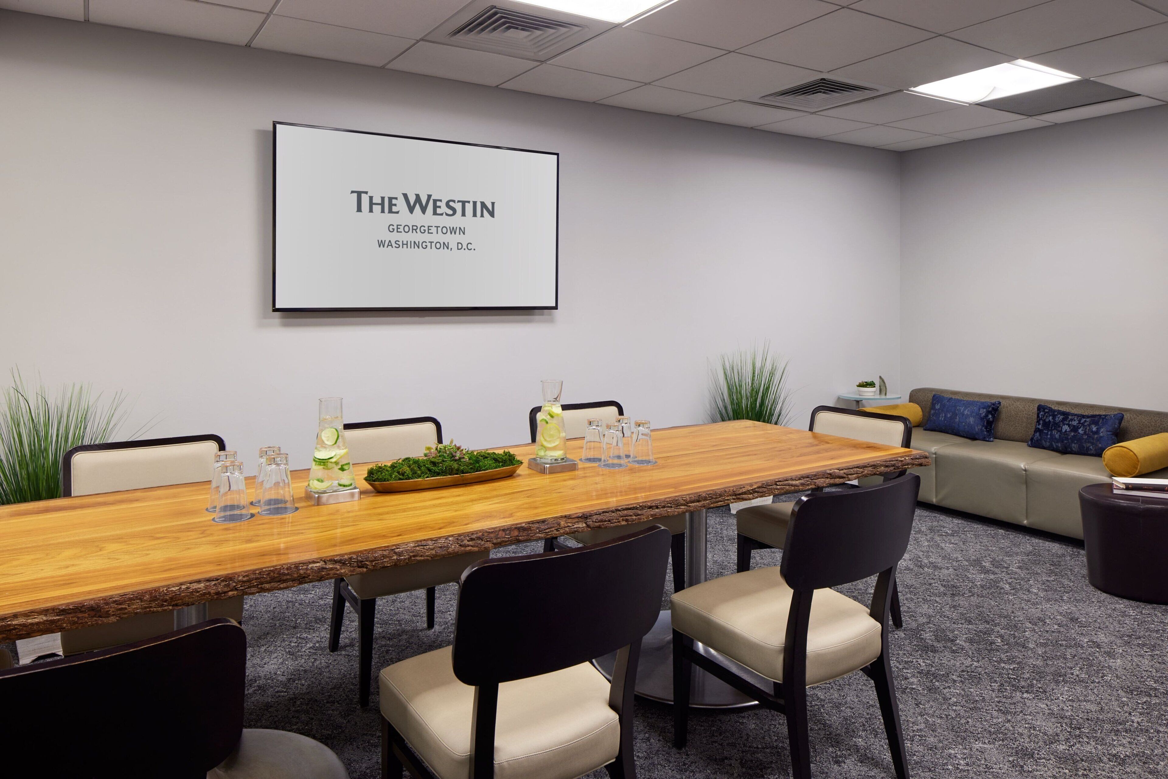 A conference room with a long wooden table, several chairs, a sofa, and a large framed sign on the wall.