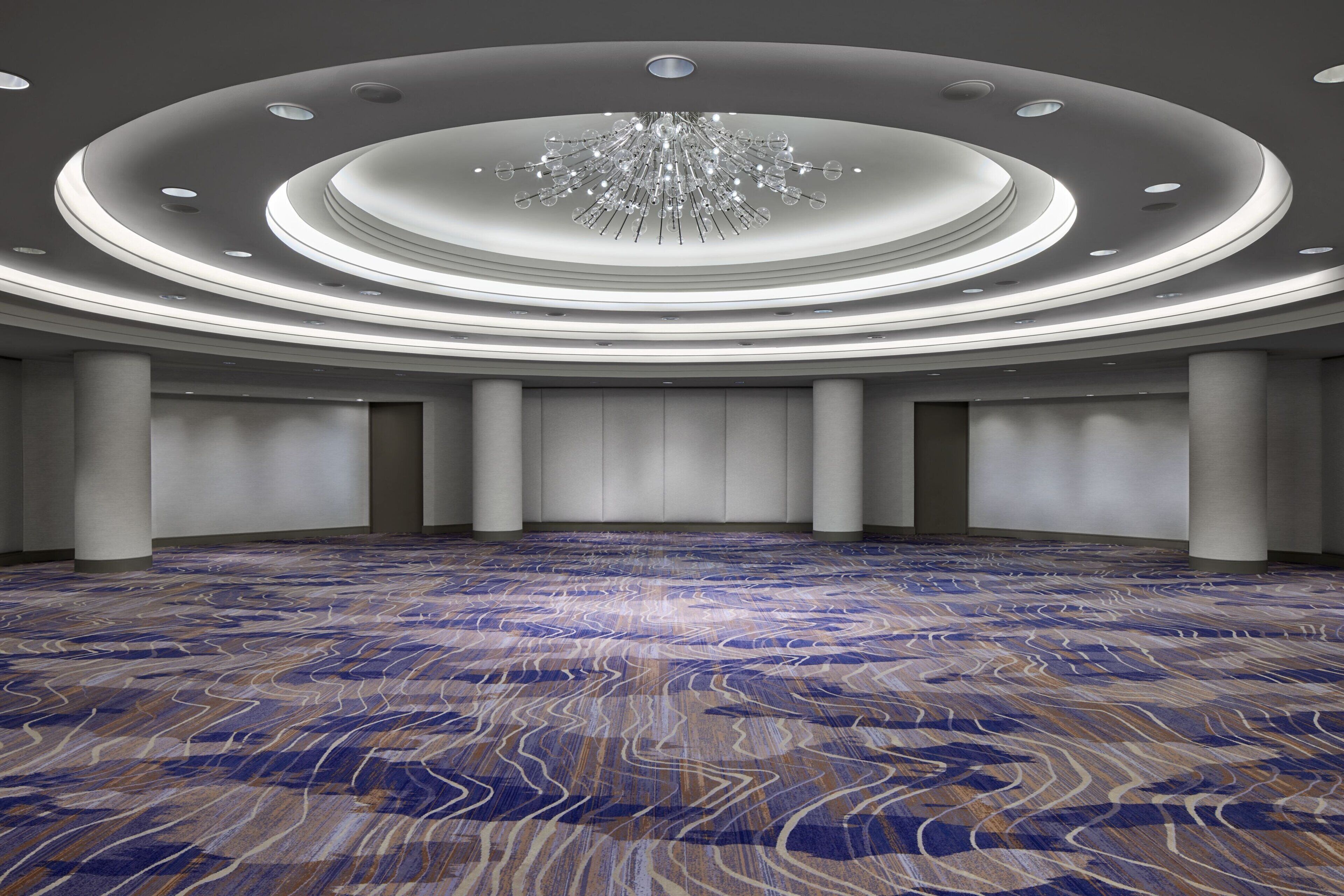 A spacious hall with a patterned carpet, a central chandelier, and a circular ceiling design.