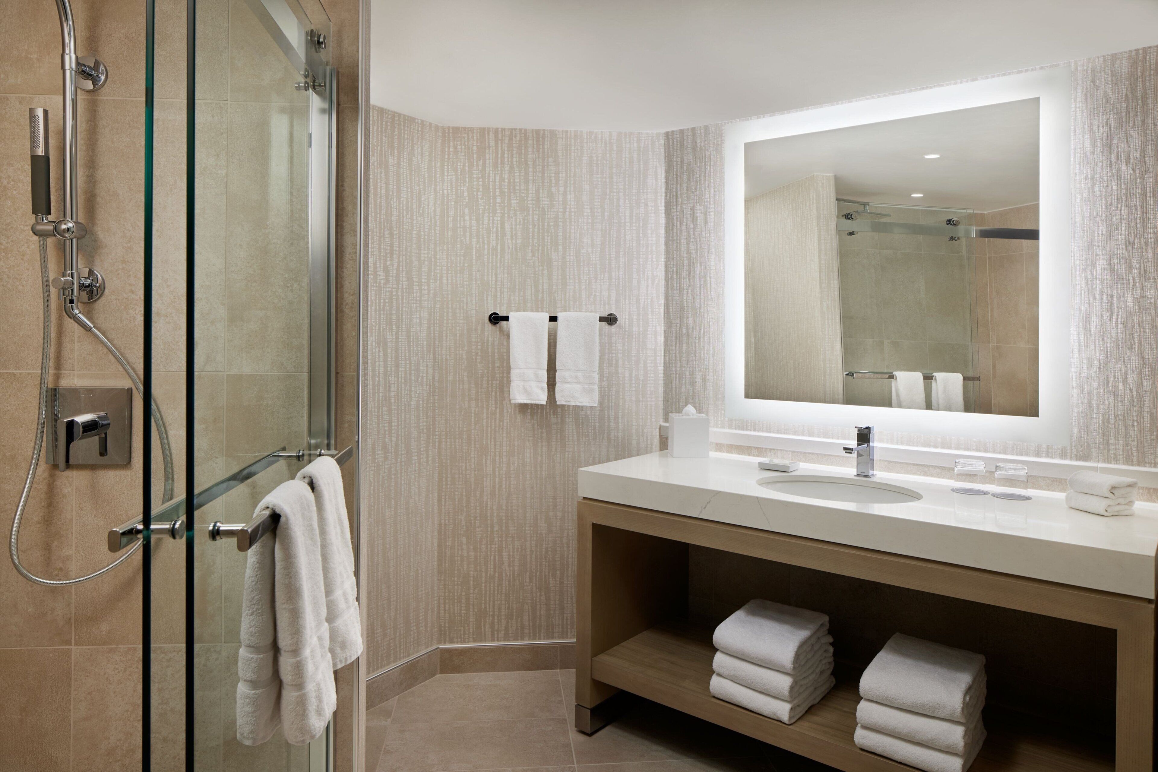 A modern bathroom with a glass shower enclosure, a large mirror, and a wooden vanity with a sink and towel storage.