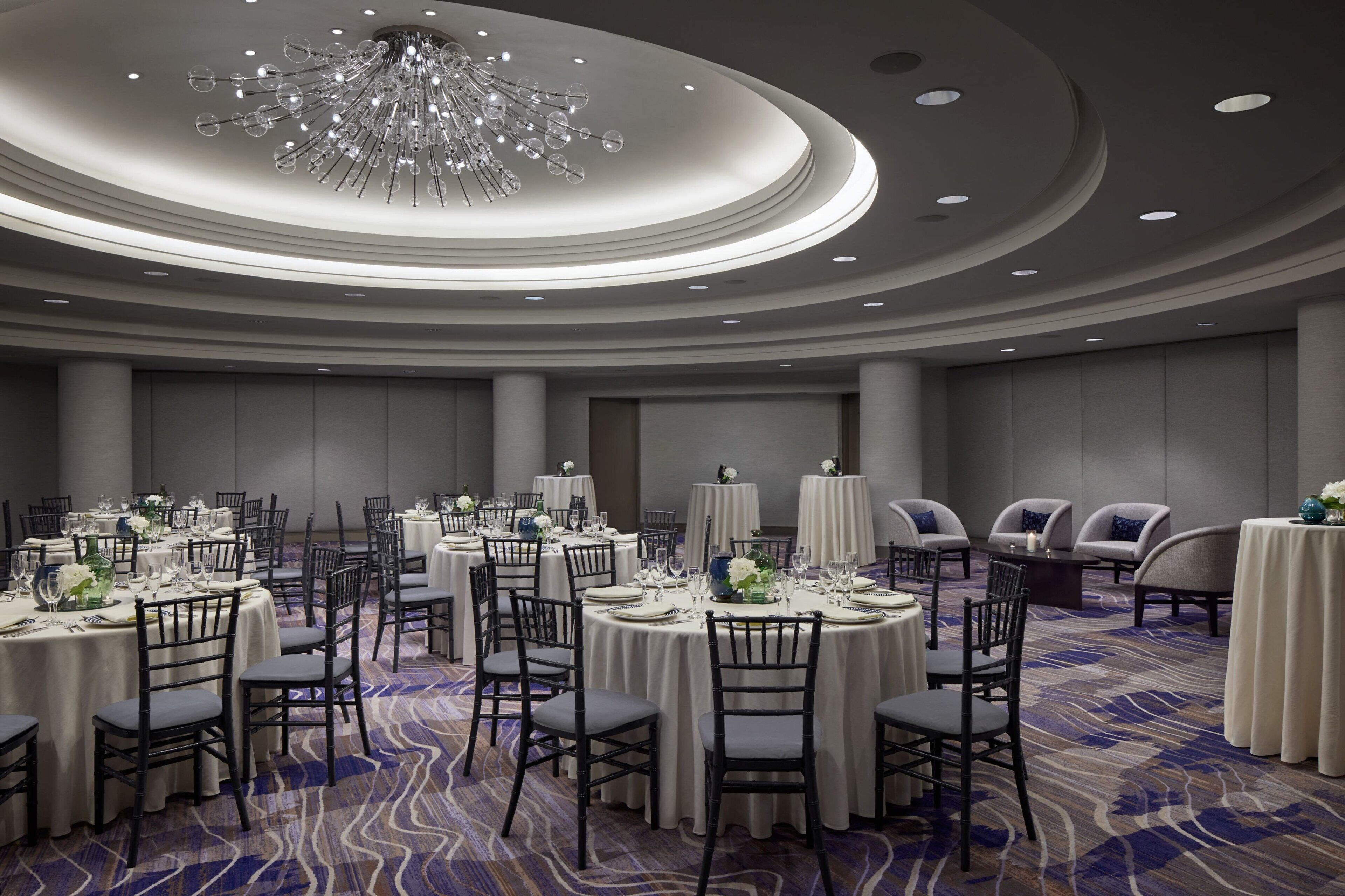 A spacious banquet hall with round tables, chairs, and a large chandelier.