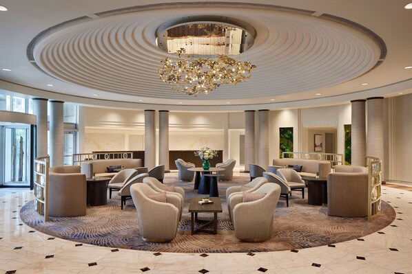 A spacious lobby with a central seating area, a chandelier, and a view of the guest elevators.