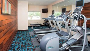 Une salle de sport équipée de tapis de course, de vélos elliptiques et d’un mur recouvert de miroirs.