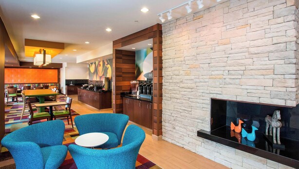Un hall d’hôtel moderne avec une cheminée en pierre, des fauteuils bleus, un coin repas et une cuisine en arrière-plan.