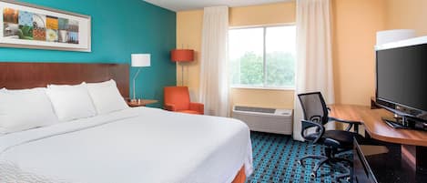 A hotel room with a large bed, a desk with a computer, a TV, and a window with curtains.