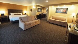A hotel room with a large bed, two sofas, a desk, and a TV. - Evergreen Resort (Cadillac)