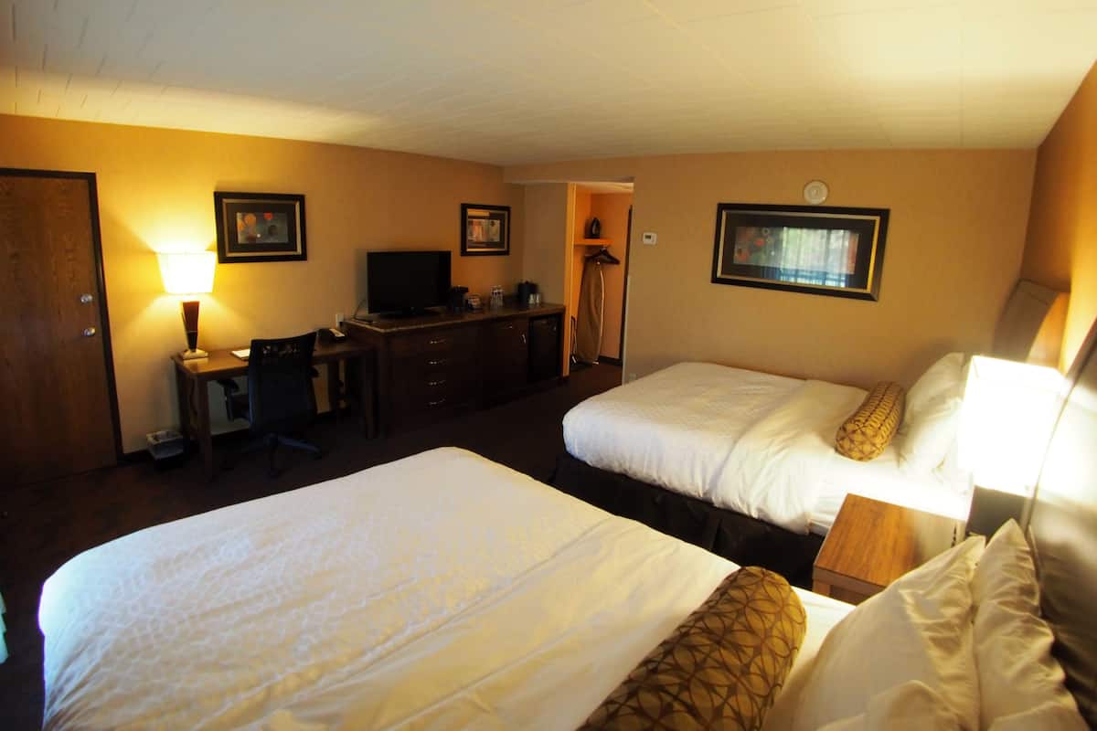 Ein Hotelzimmer mit zwei Betten, einem Schreibtisch mit Lampe, einem Fernseher und einem Kleiderschrank.