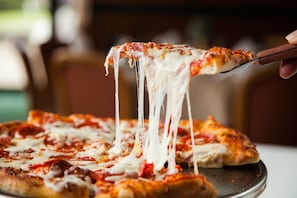 Primer plano de una pizza con queso derretido que se levanta con una espátula.